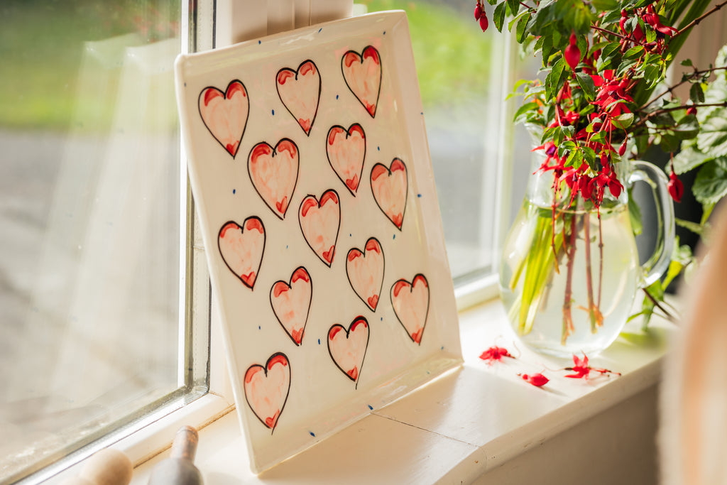 Large serving plate with pink Grá heart designs on a luxurious white glaze with periodic blue dots  