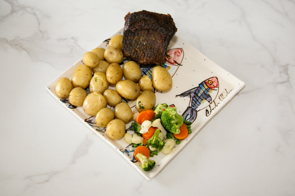 Platter with potatoes, meat, and vegetables on a decorative plate with hand painted mackerel fish  .