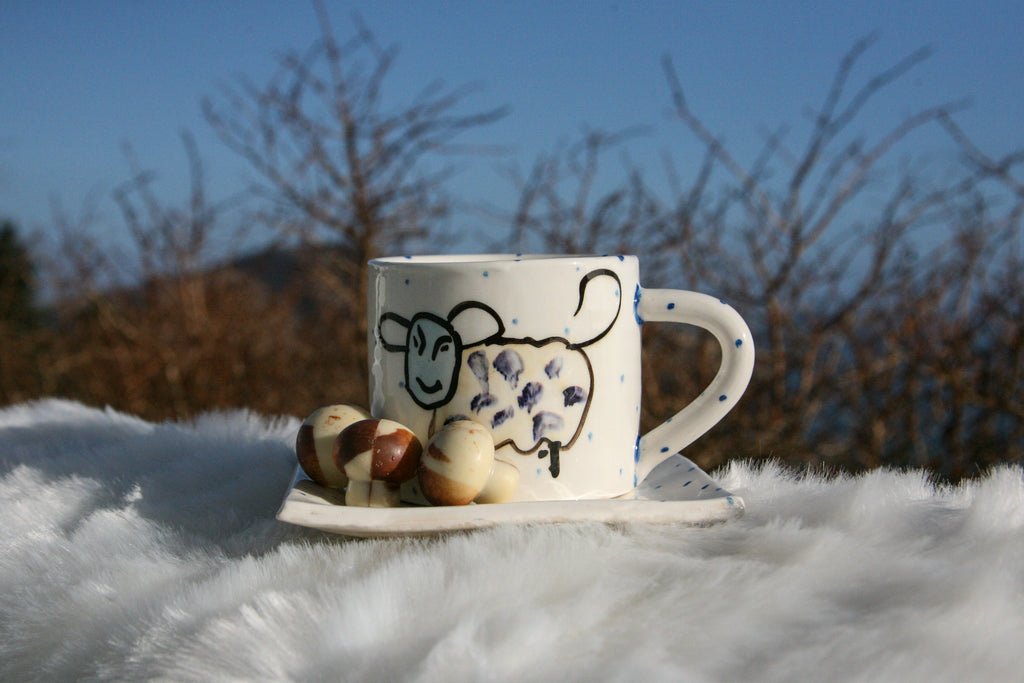 large Irish ceramic mug with sheep design and periodic blue polka dots sitting on a plate with same design 