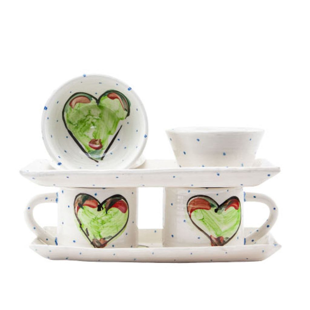 Two handmade pottery mugs with green hearts handpainted resting on a rectangular plate with another rectangular plate resting atop the mugs displaying two coordinating handmade bowls.