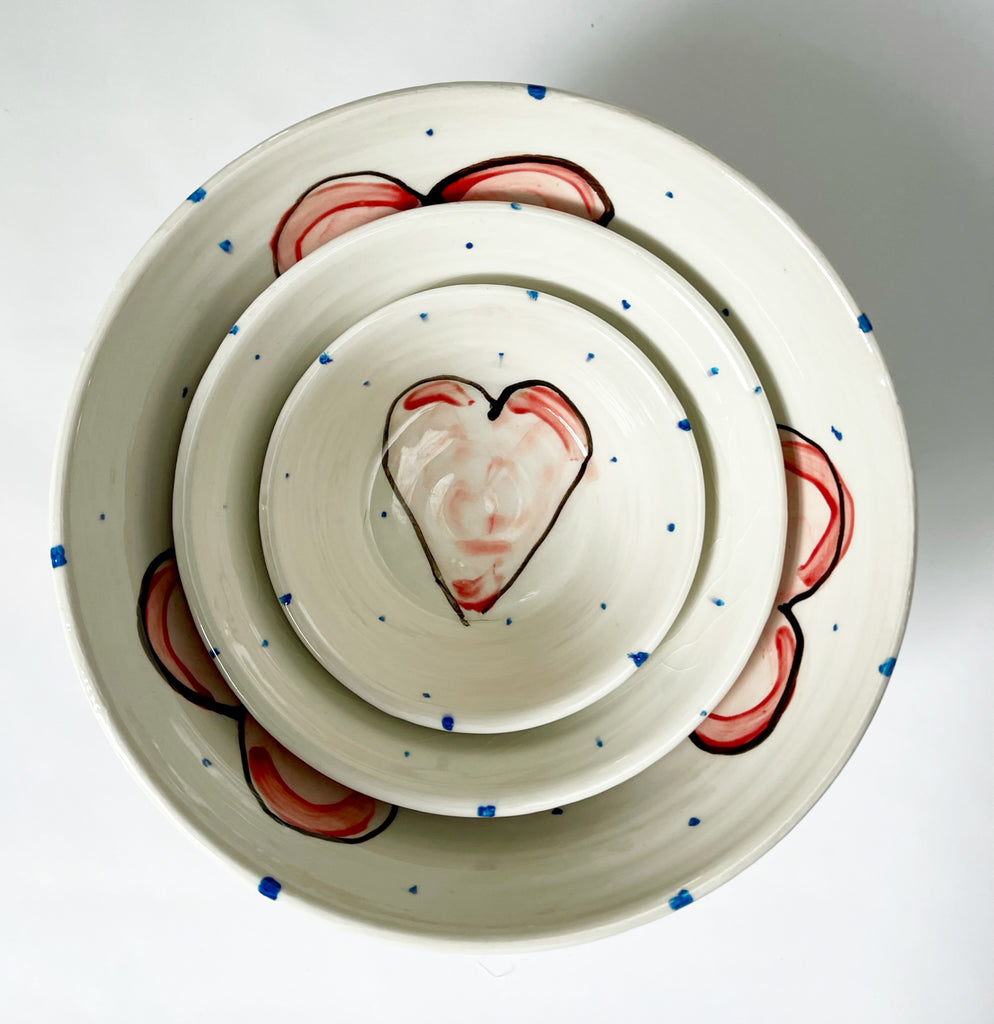 Three bowls nesting together, a dipping bowl, a breakfast bowl, and a salad bowl - all handmade and hand painted with periodic blue dots and pink hearts 