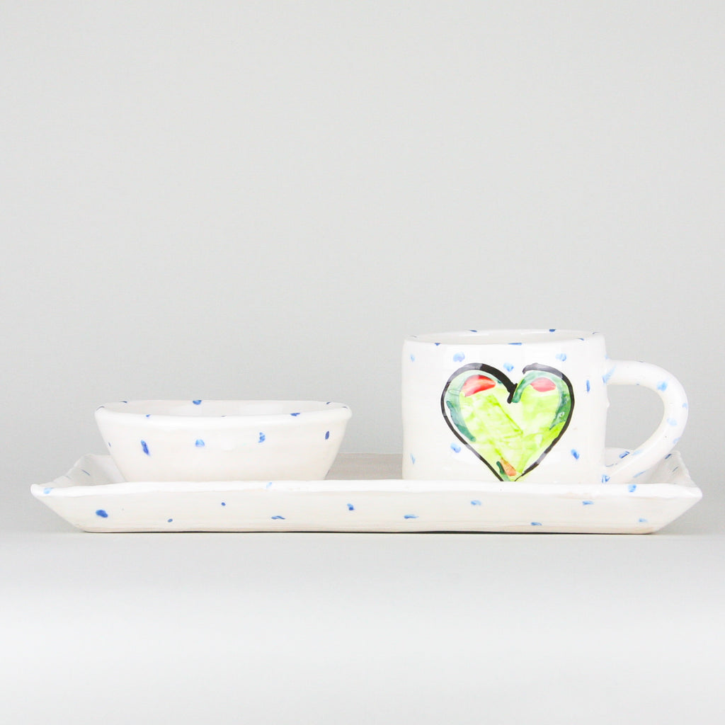 Green heart rectangular platter and mug set. The mug sits on the right heart of the platter and handle facing right. Blue dots pepper the handmade Irish pottery. A ramekin bowl rests on the left side of the platter.