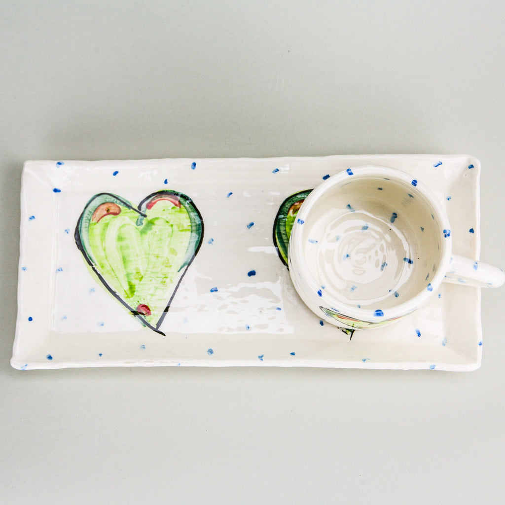 Green heart rectangular platter and mug set. An aerial view with the mug sitting on the right heart of the platter and handle facing right. Blue dots pepper the handmade Irish pottery.