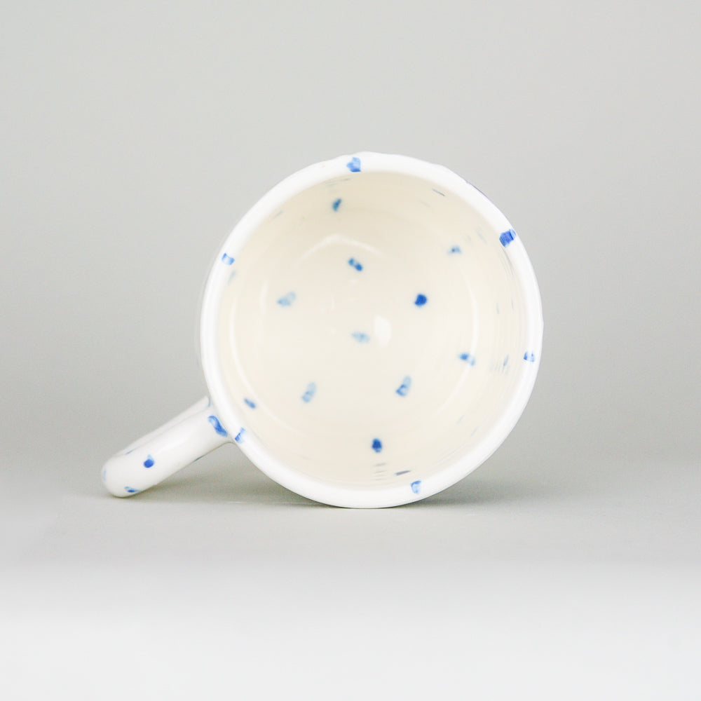 A peek inside a handmade pottery mug. Crisp white Irish pottery with little blue dots hand-painted along with a smiling mackerel fish.