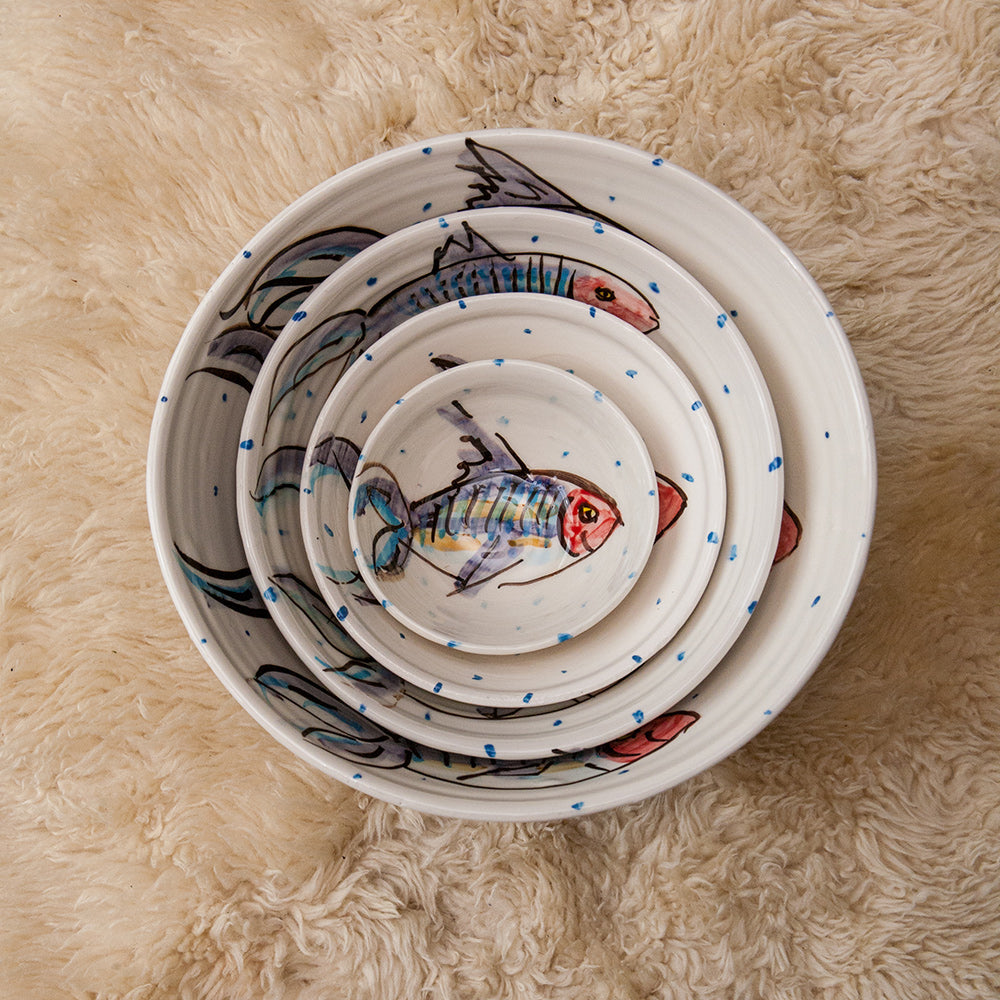 Four sizes of mackerel bowls nested together, from the ramekin to the small bowl, medium bowl, and the large bowl. Each is hand-painted with the smiling mackerel fish motif unique to Charlie Mahon. Handmade in Ireland.